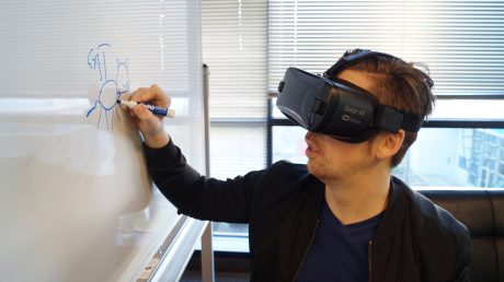 person wearing black vr box writing on white board